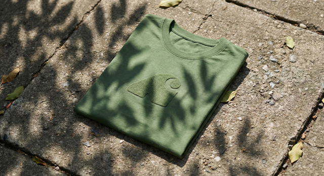 Deep moss green Forest Felt 041 t-shirt folded on raw concrete sidewalk with dappled komorebi sunlight shadows