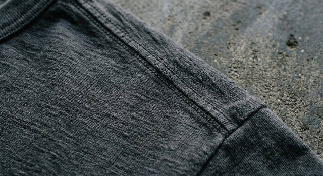 Extreme close-up of charcoal grey cotton t-shirt fabric and seam resting on a concrete surface.