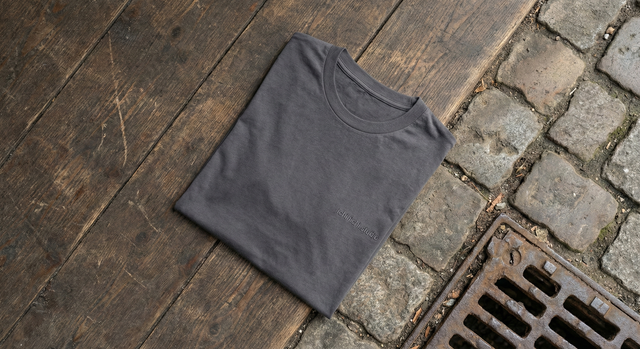 Top-down photograph of a folded t-shirt resting on a surface that is half worn wooden planks and half rough cobblestones with cast iron.