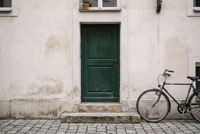 A bicycle stands beside a pale Munich facade with a stone threshold and dark green door.