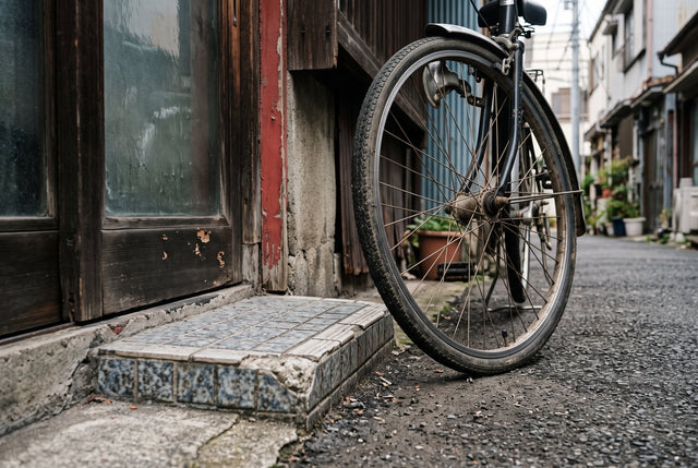 A close view of a tiled Tokyo doorway, a bicycle wheel, and a narrow strip of red paint.