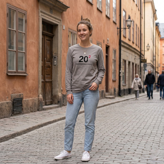 Woman wearing a gray sweatshirt with '2021' printed on it, standing on a cobblestone street.