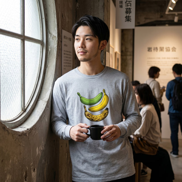 Man wearing a gray t-shirt with banana design, holding a mug, standing indoors.