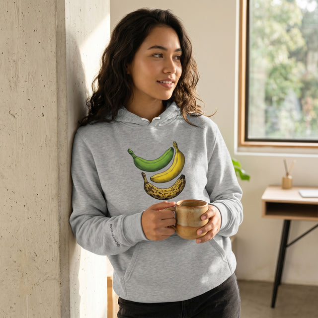 Woman wearing a hoodie with banana design, holding a mug indoors.