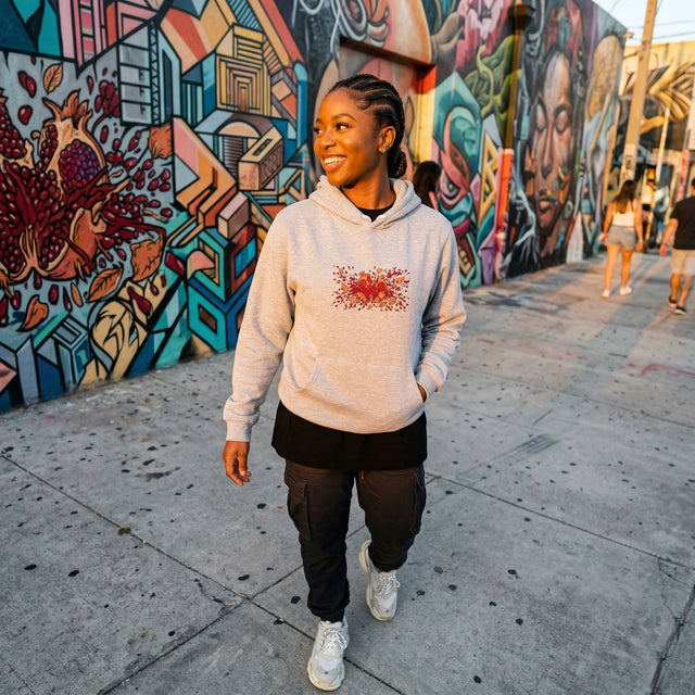 Person wearing a light gray hoodie with a red design, standing in front of colorful graffiti art.