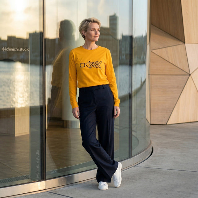 Person wearing a yellow sweater with a black design, standing in front of a modern glass building.