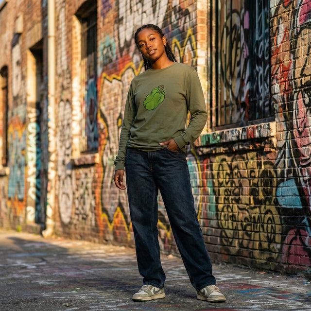 Person wearing a green sweater with a graphic design, standing in front of a graffiti-covered wall.