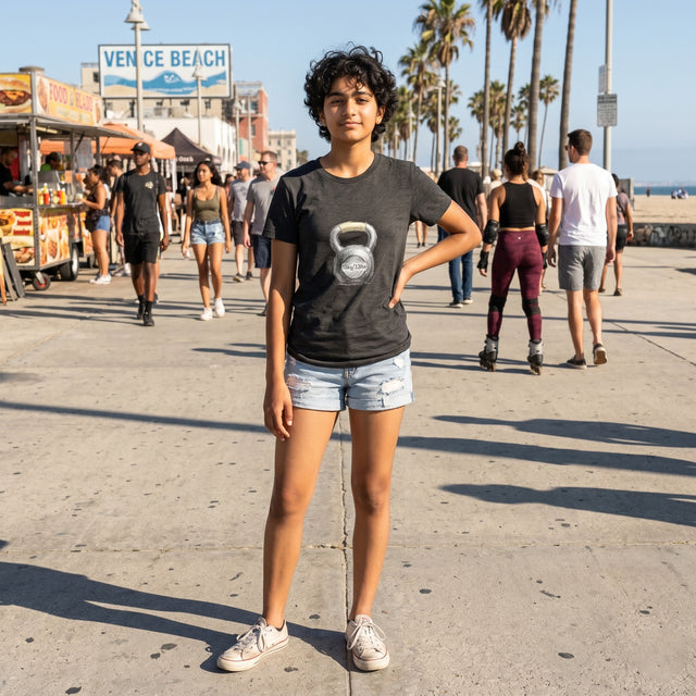 Person wearing a black t-shirt with a kettlebell graphic on a Venice Beach boardwalk.