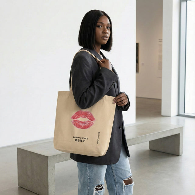 Model holding oyster eco tote bag with red lipstick kiss mark illustration and Japanese text Leave a mark in modern art gallery setting.