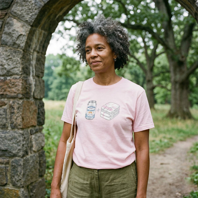Woman wearing a pink t-shirt with a graphic design, standing under a stone archway in a park.