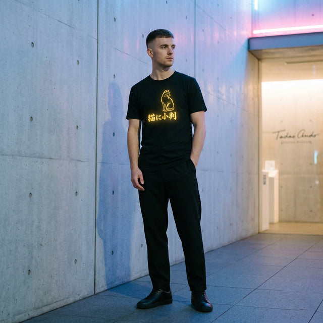Man wearing a black t-shirt with a yellow graphic design standing against a modern building exterior.