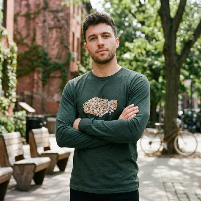 Man wearing a green long-sleeve shirt with a graphic design, standing outdoors with trees and benches in the background.