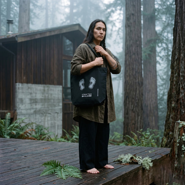 Person holding a black bag with footprints in a forest setting