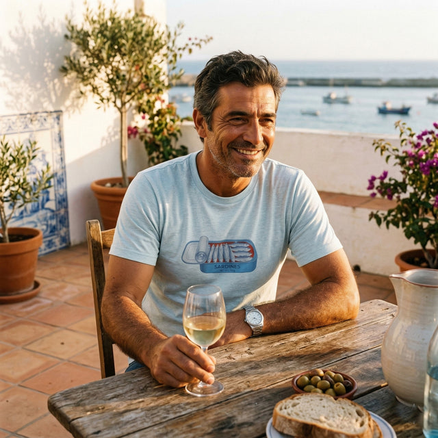 Man sitting at a table with a glass of wine, smiling on a terrace with a scenic view.