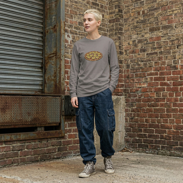 Person wearing a gray long-sleeve shirt with a logo and blue jeans standing against a brick wall.