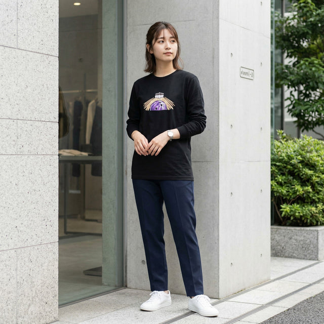 Woman wearing a black sweatshirt with a graphic design, navy pants, and white sneakers standing outside a building.