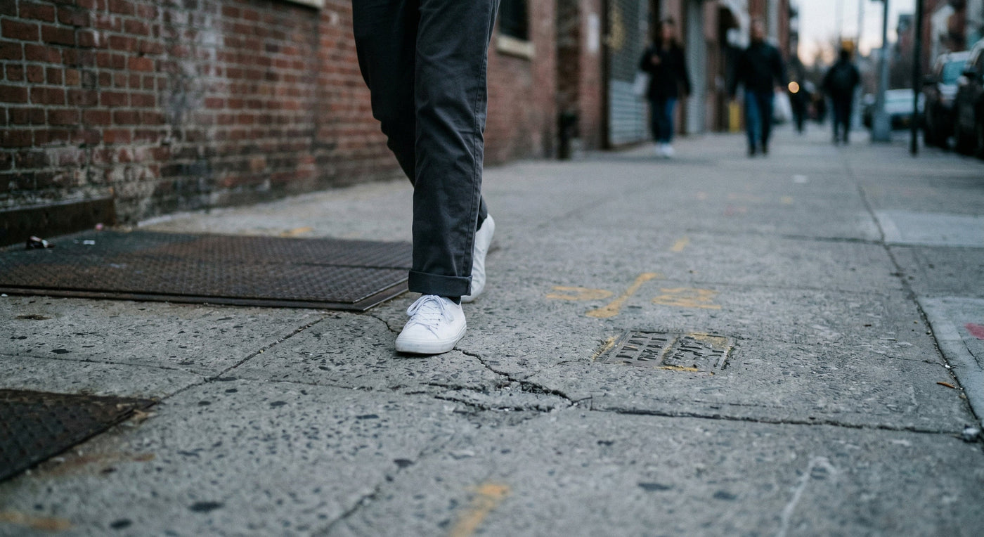 A low-angle shot of someone walking on a gritty concrete sidewalk in Brooklyn, emphasizing the textures of the city.