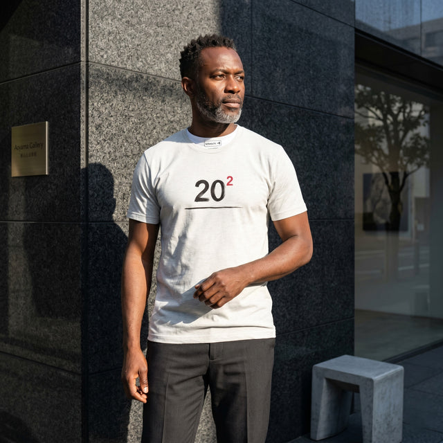 Man wearing a white t-shirt with '20²' design standing against a building.