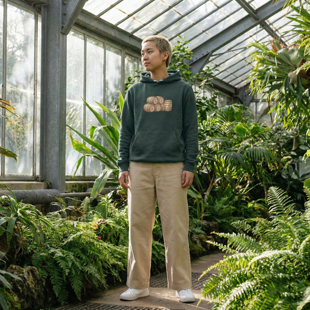 Person wearing a hoodie with text in a greenhouse filled with plants