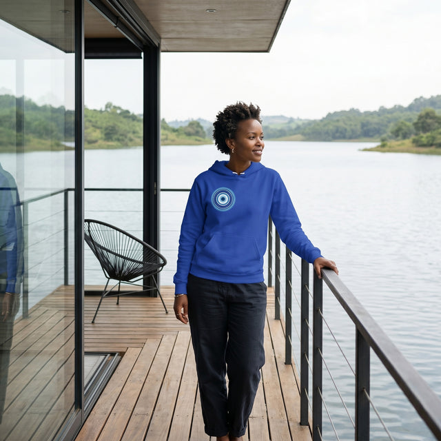 Person wearing a blue hoodie with a circular design, standing on a wooden deck by a body of water.