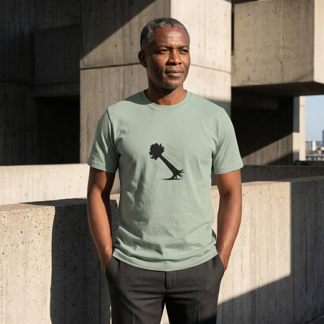 Man wearing a light green t-shirt with a black graphic design, standing against a concrete wall.