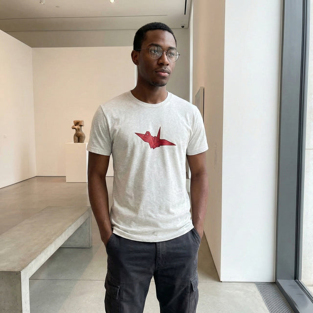 Ichinichi unisex staple t-shirt in ash grey featuring a red origami crane graphic, modeled in a minimalist modern art gallery, Japanese streetwear fashion.