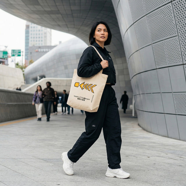 Person walking outdoors holding a beige tote bag with text and graphics.