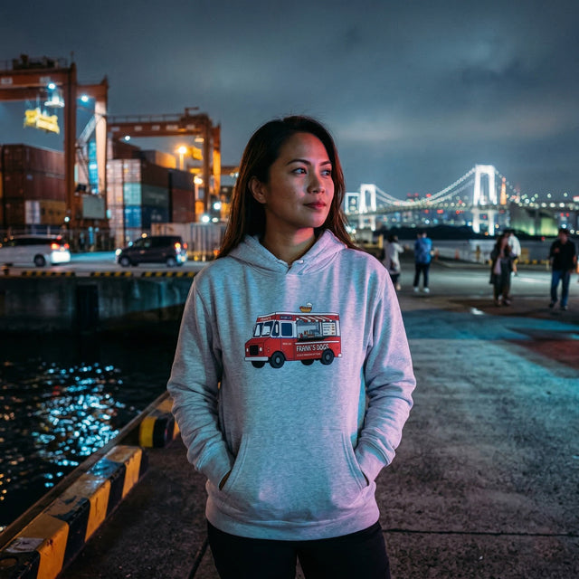 Person wearing a hoodie with a red bus graphic in an urban night setting with a bridge in the background.