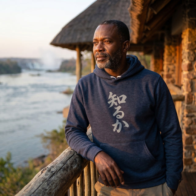 Man wearing a hoodie with text standing by a scenic waterfront.