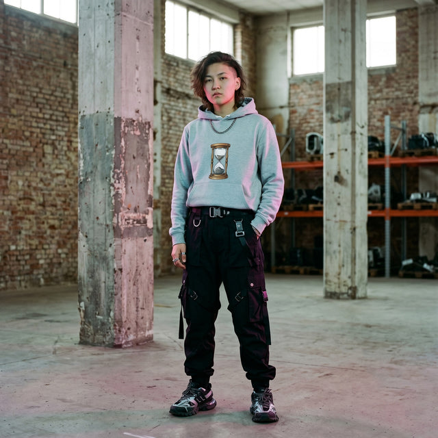 Person wearing a light blue hoodie with a design and dark pants in an industrial setting.