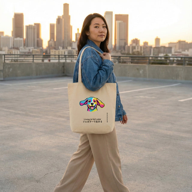 Beige canvas tote bag with colorful pop-art puppy and "Living in full color" text, held by a woman on a city rooftop parking garage at sunset.