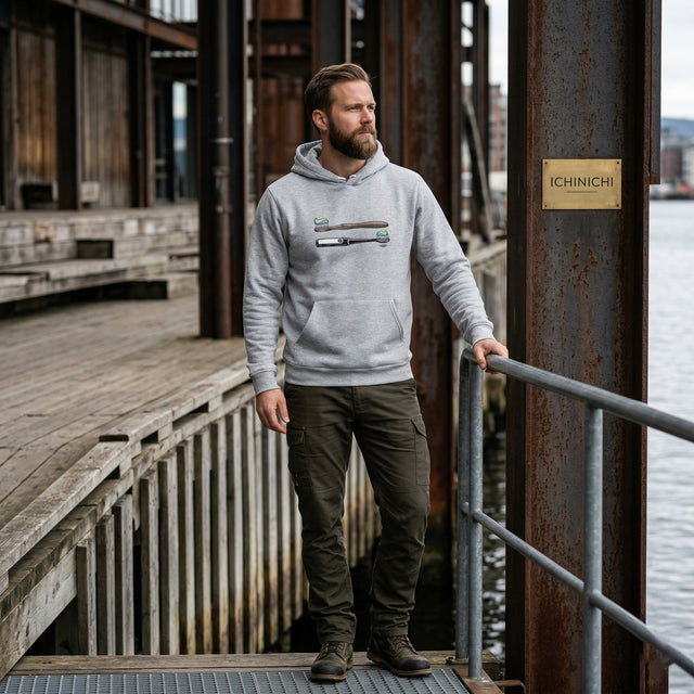 Man wearing a gray hoodie with a logo standing on a dock by water.