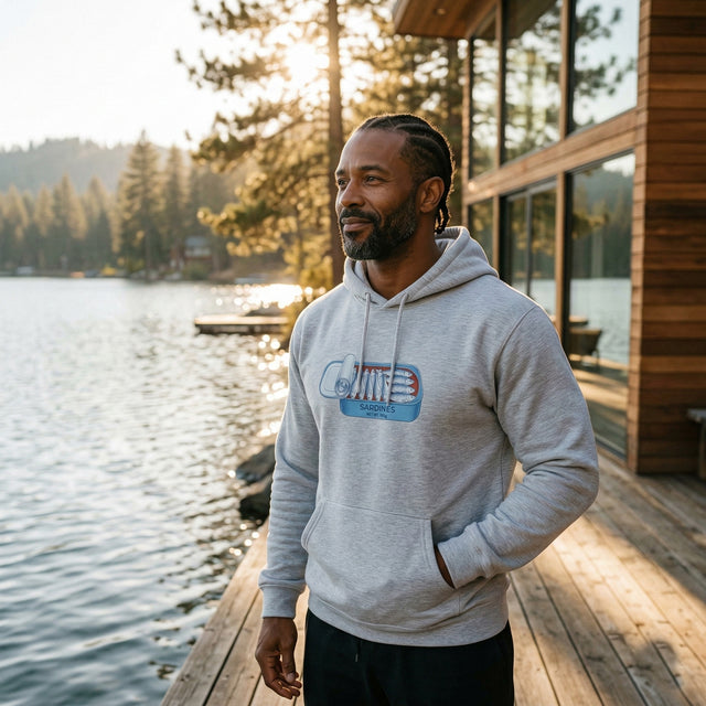 Man wearing a hoodie with a graphic design by a lake and cabin