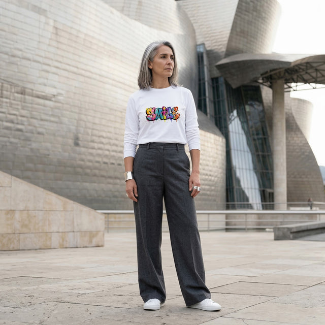Person wearing a white sweatshirt with colorful text in front of a modern building.