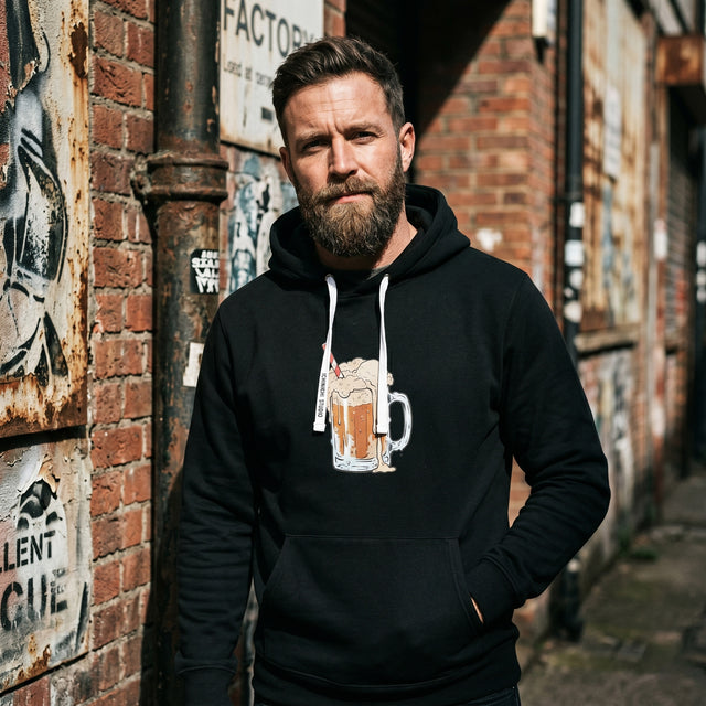 Man wearing a black hoodie with a graphic design standing against a brick wall with graffiti.