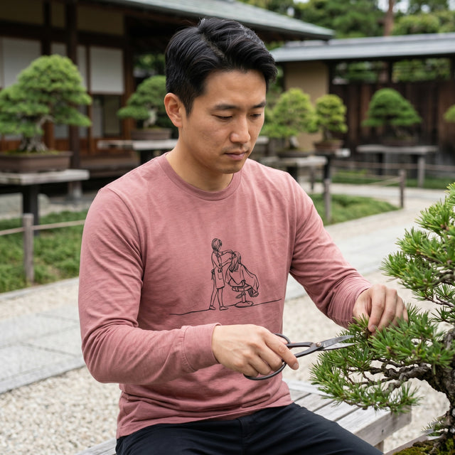 ピンクのシャツを着た男性が、屋外で盆栽の手入れをしている。
