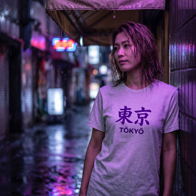 Man wearing a white t-shirt with 'TOKYO' printed on it, standing in a modern building with cityscape view.