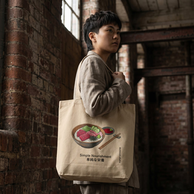 Person holding a tote bag with a bowl of sushi design against a brick wall.