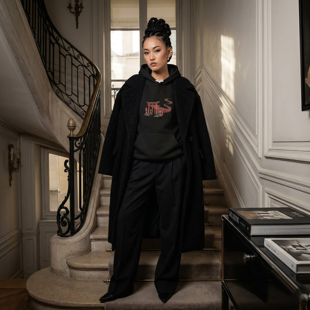 Woman in a black outfit with a red logo standing on a staircase in an elegant interior setting.