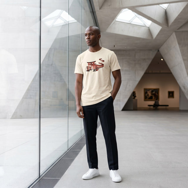 Man wearing a beige t-shirt with a graphic design in an indoor setting with modern architecture.