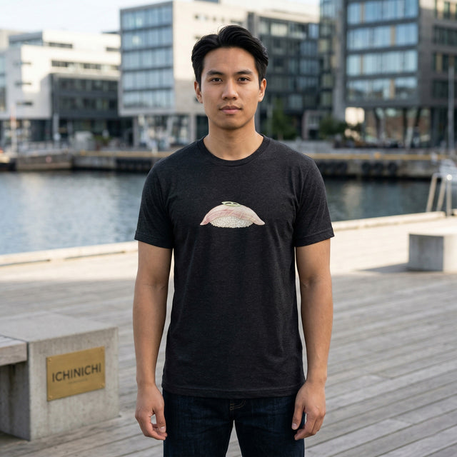 Man wearing a black t-shirt with a graphic design standing on a dock with buildings and water in the background