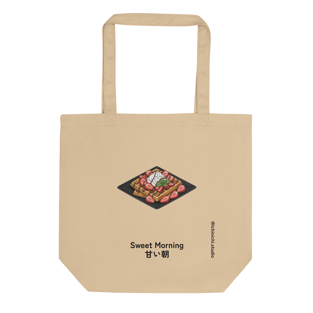 An eco tote bag featuring a bird's-eye view brush pen graphic of waffles on a black plate with whipped cream and strawberries.